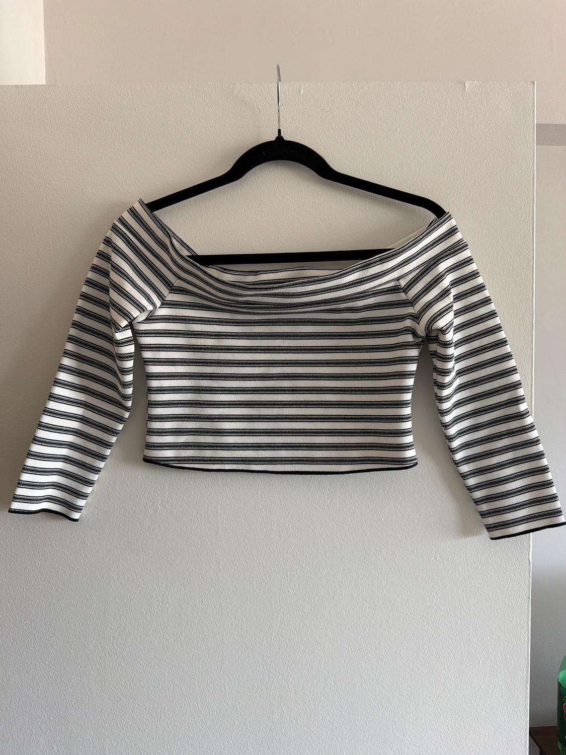 Black and white striped off-the-shoulder long-sleeved top, hanging on a black hanger against a white wall.
