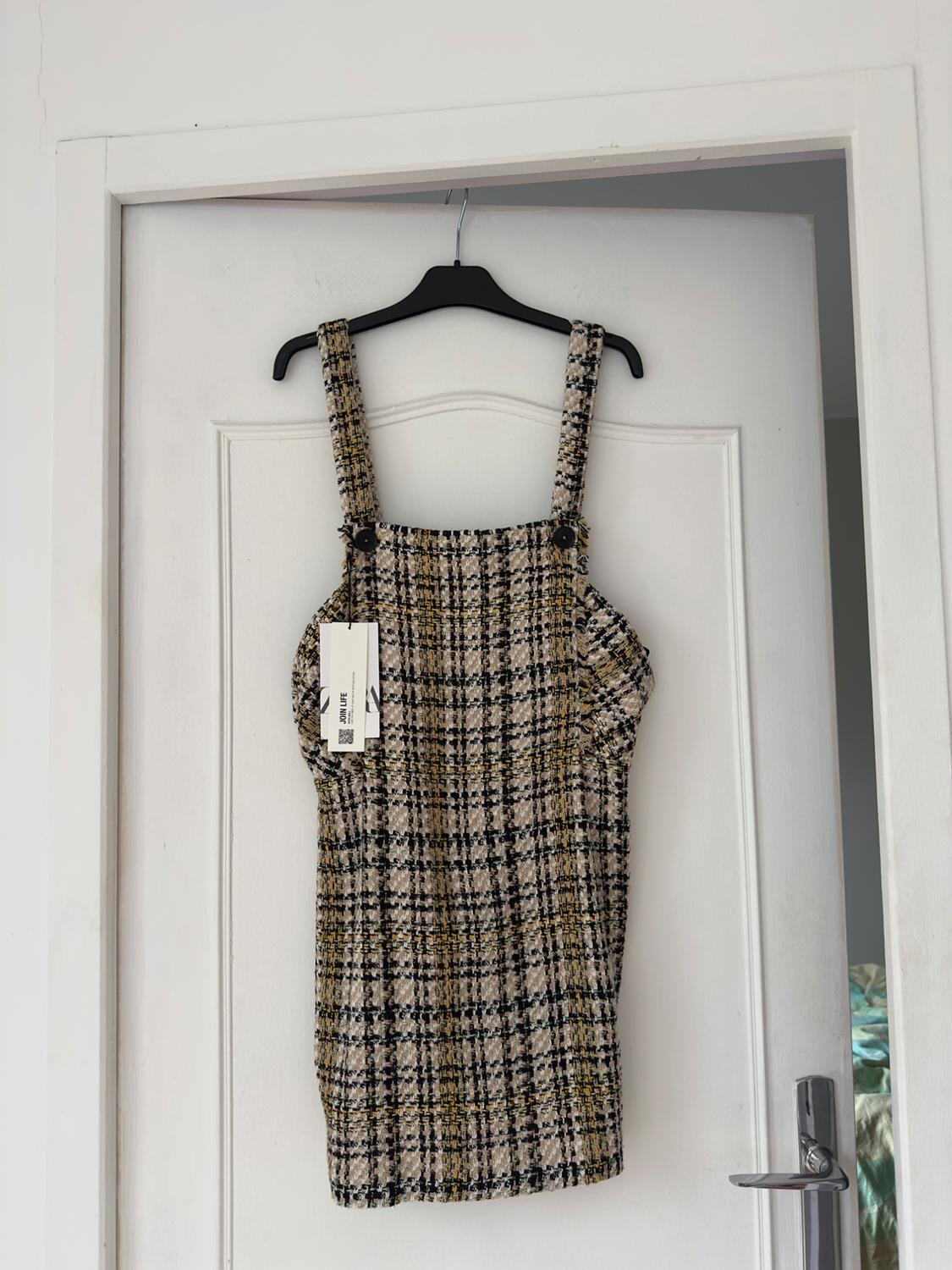 Strappy checked dress in beige and black tones, hanging on a black hanger over a white door.