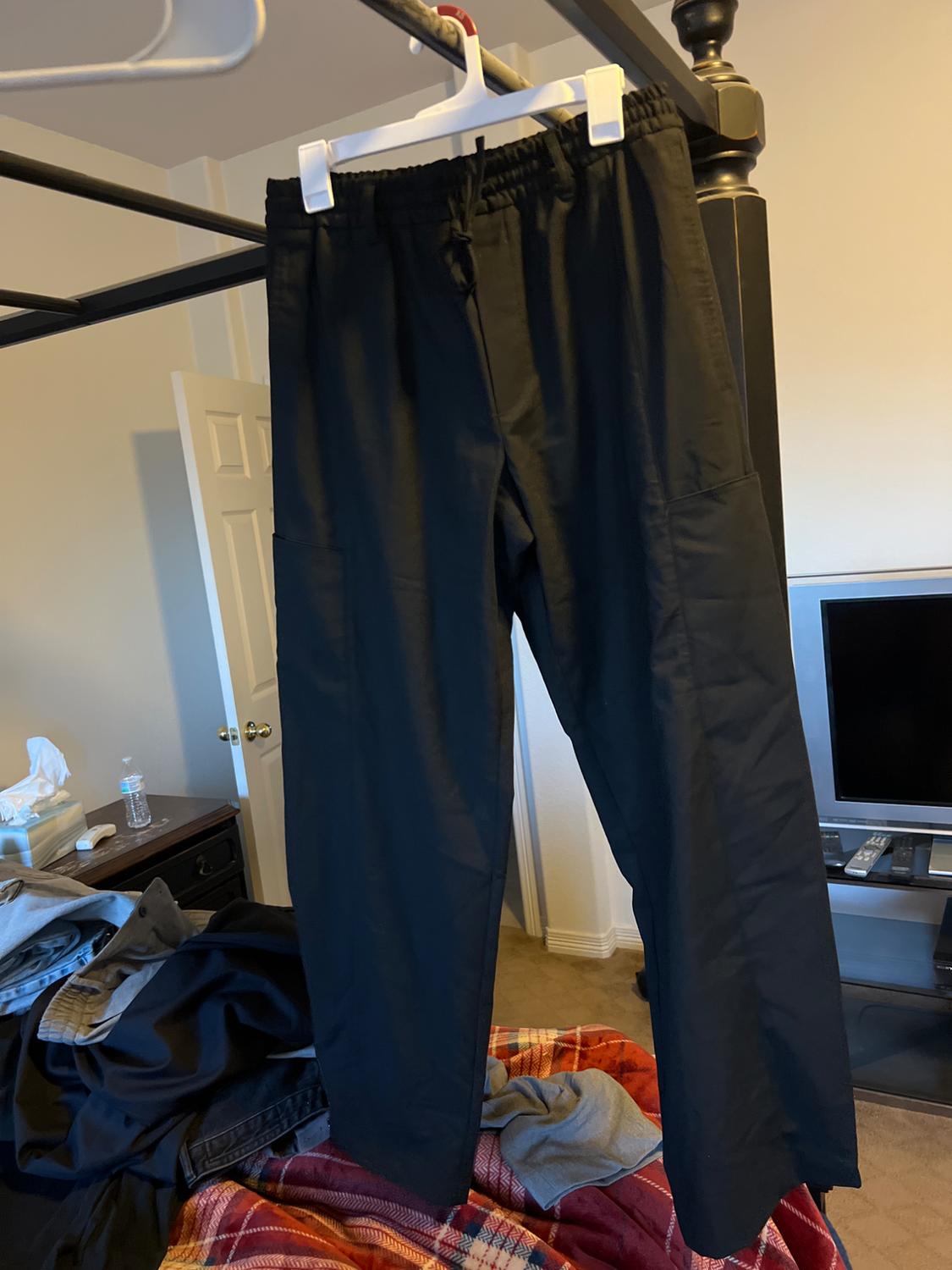 Front view of black pants with elastic waistband and side pockets hanging on a hanger.