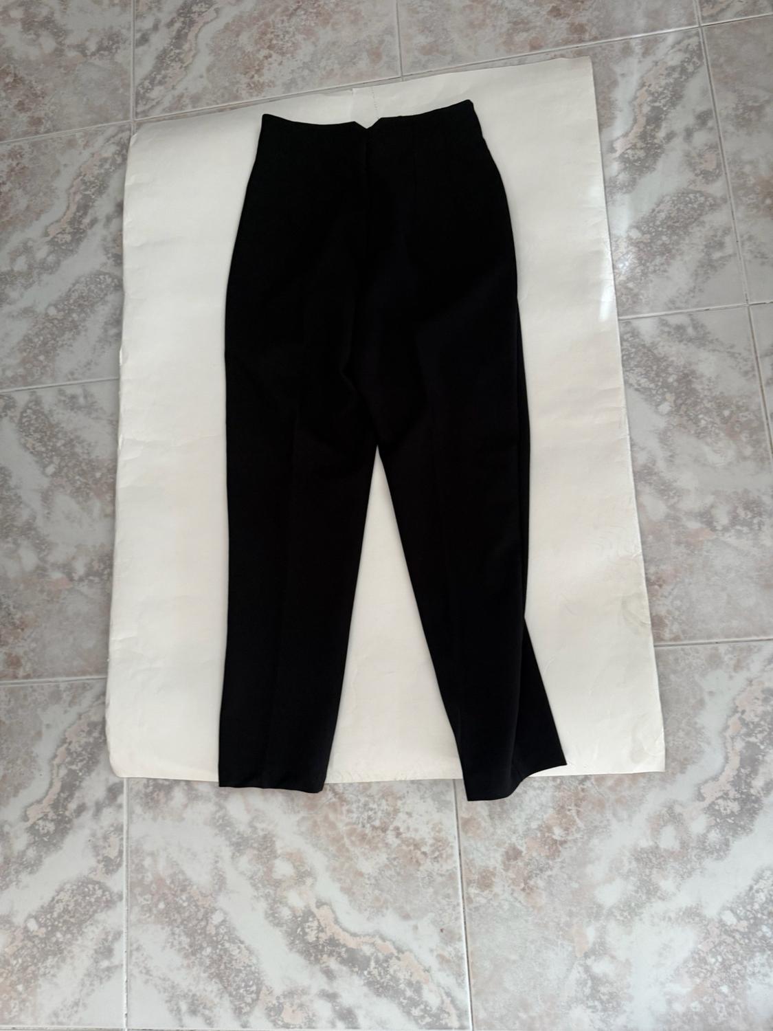 Black trousers laid out on white paper on a light marble-effect tiled floor. Casual style composition.
