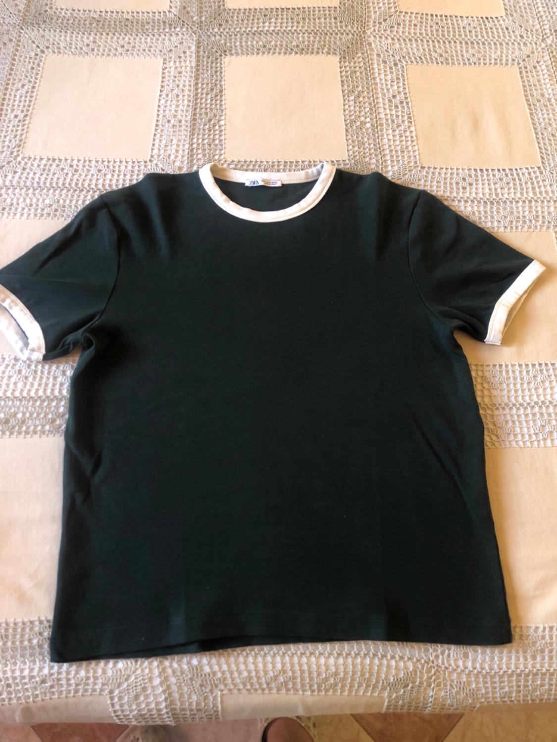 Black T-shirt with white trim on the collar and sleeves, on a beige and white checked tablecloth.