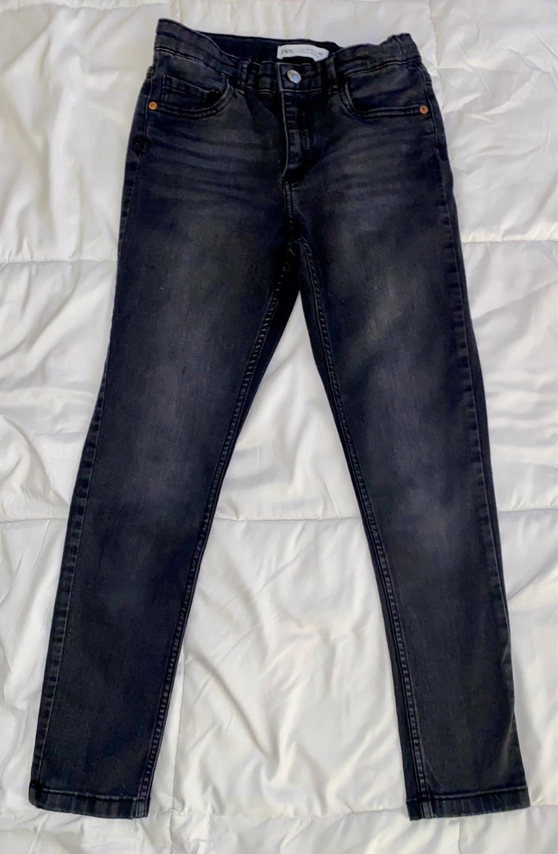 Front view of black jeans with front pockets and visible button.