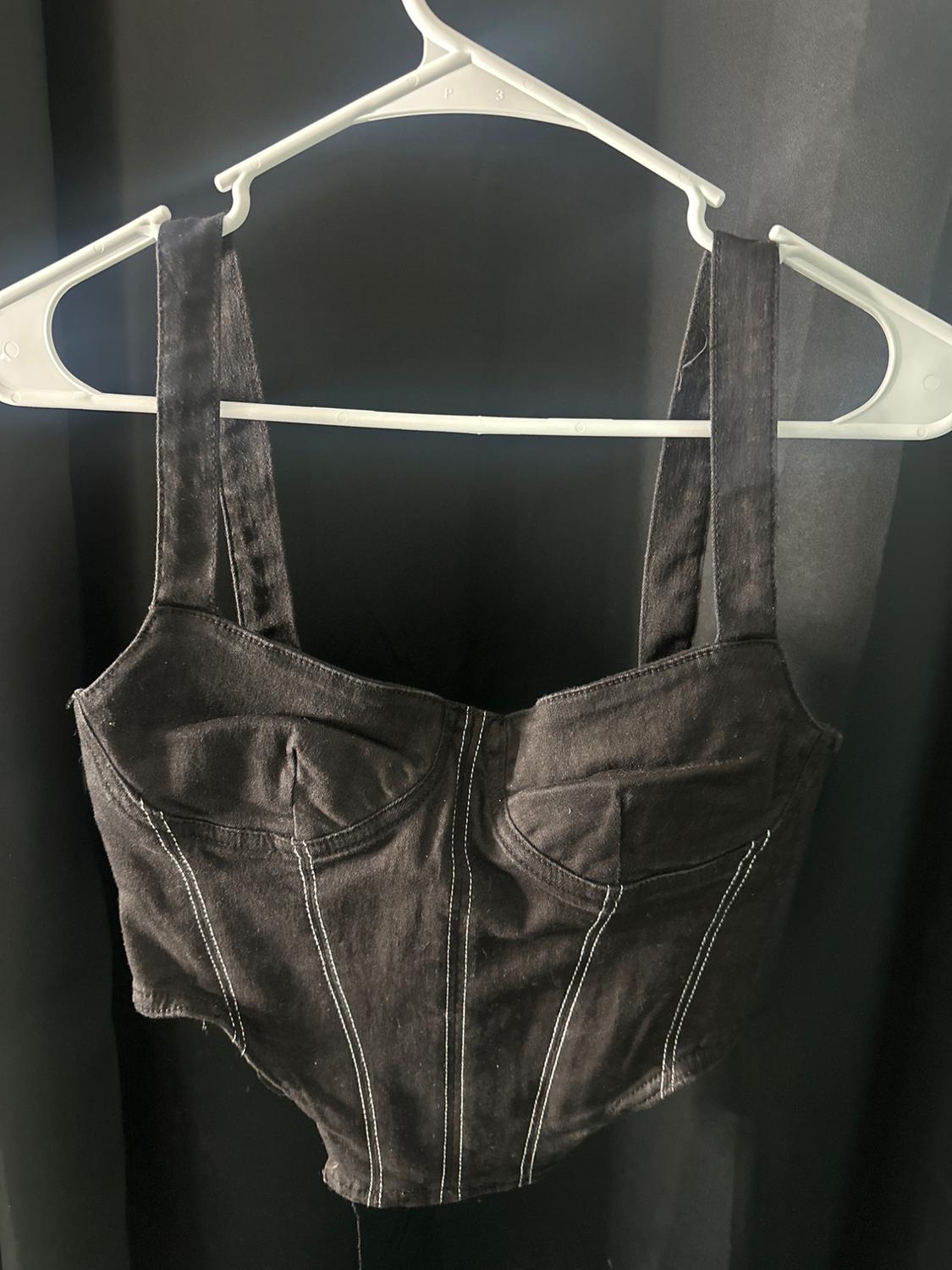 Black tank top with wide straps and visible white stitching, hanging on a white hanger against a dark background.