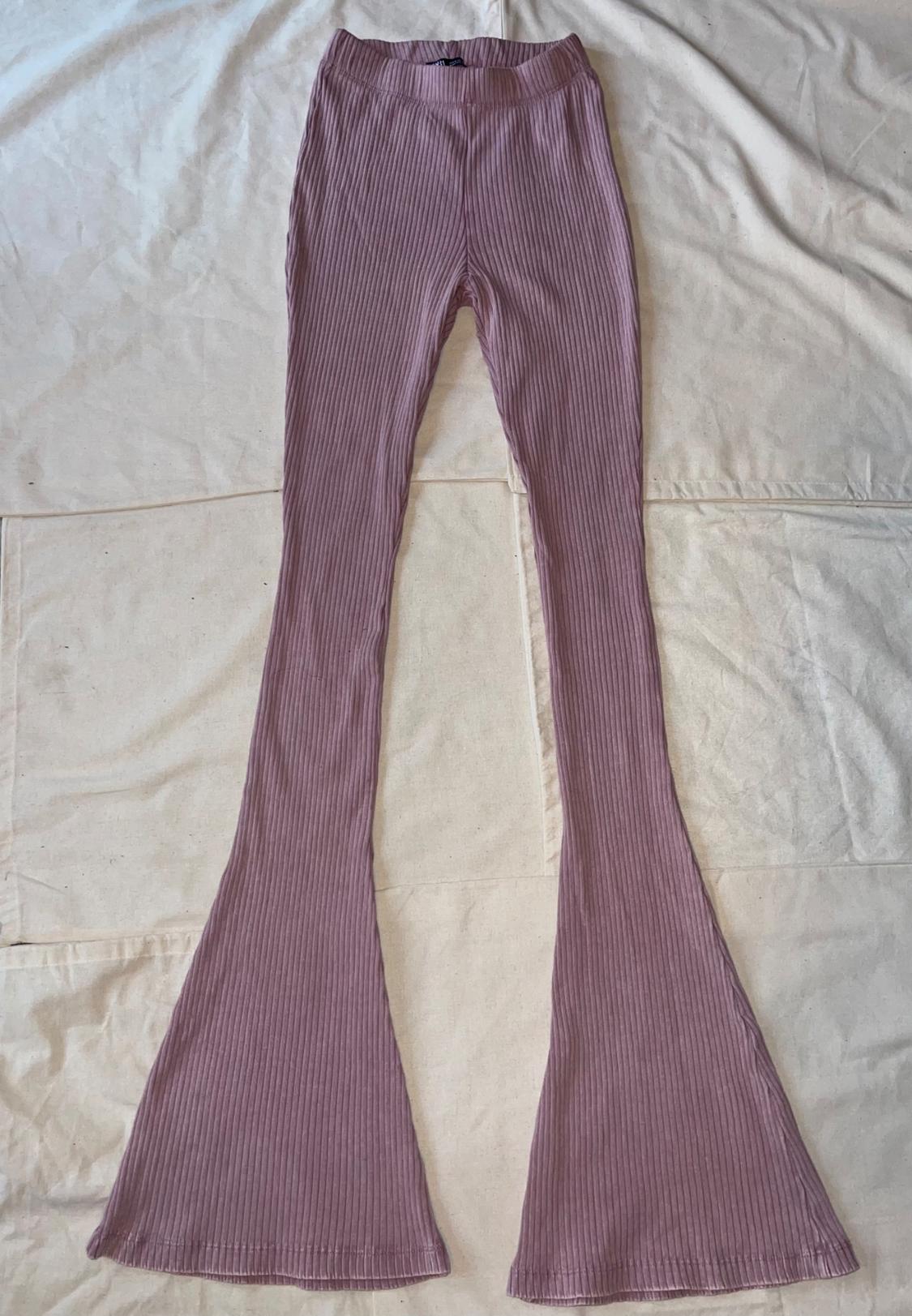 Dusty pink ribbed flared-hem pants, laid out on a wrinkled light-colored fabric background.