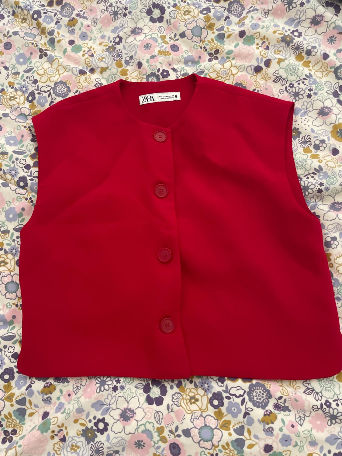 Red sleeveless waistcoat with buttons over floral fabric in pastel shades. Visible label: "ZARA".