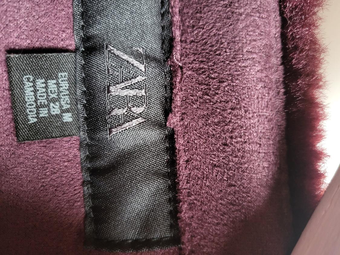 Close-up of a black label on burgundy textured fabric. Text: ZARA, EUR/USA M, MEX 28, MADE IN CAMBODIA.