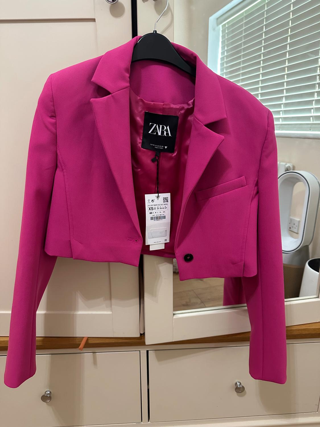 Fuchsia ZARA short jacket hanging on a black hanger in front of a white wardrobe. Visible label with size XS.