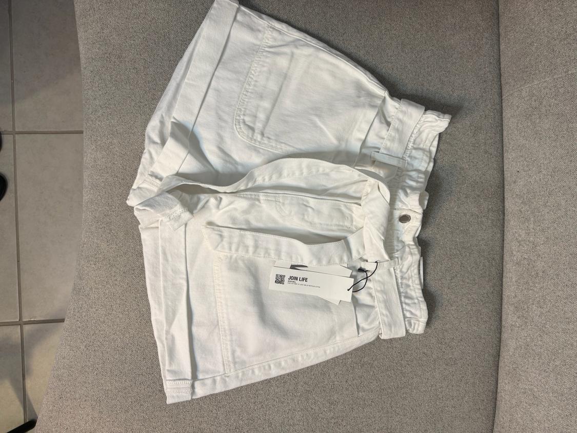 White denim shorts with a belt and pockets on a grey surface. Label with the text JOIN LIFE.