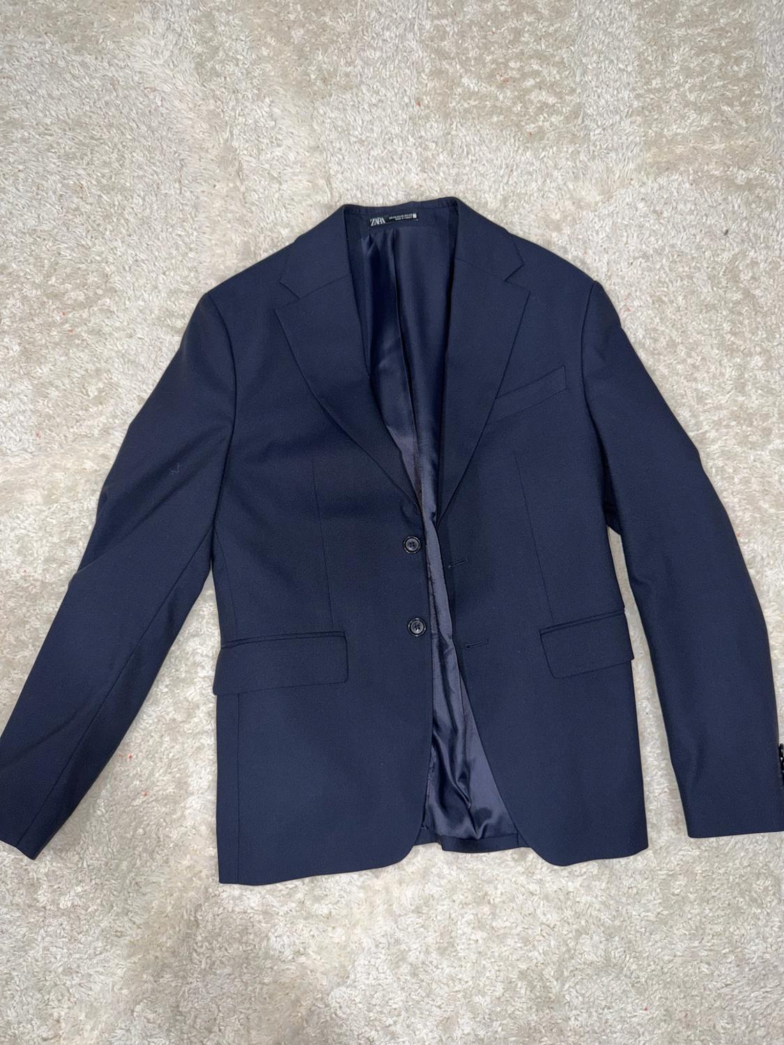 Navy blue two-button jacket, open to show the ZARA label, arranged on a textured white carpet.