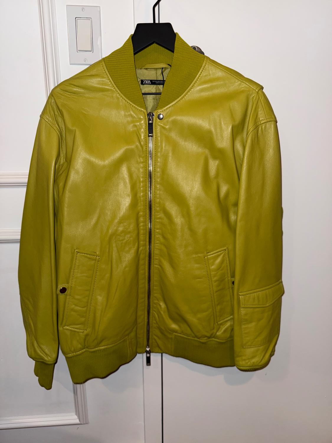 Lime green bomber jacket with front zip fastening, side pockets, and knitted collar, cuffs and hem, hanging on a black coat hanger.