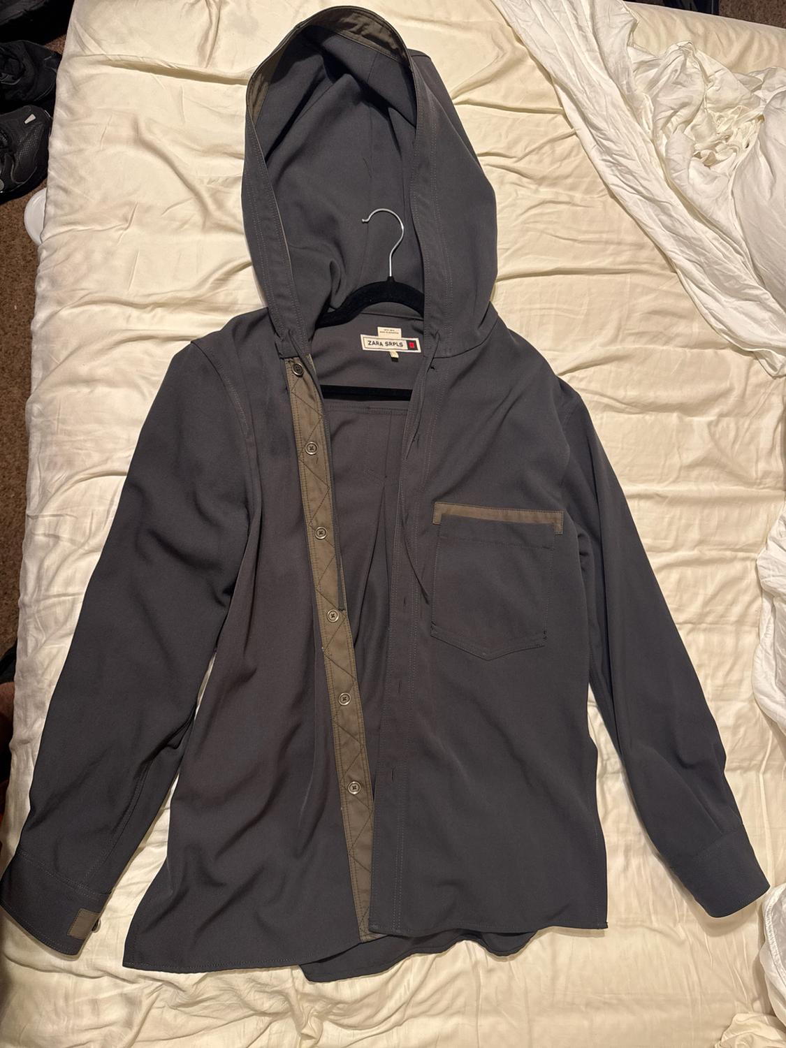 Gray hoodie shirt, long sleeves, button-front closure with padded detailing, and a chest pocket. The "ZARA SRPLS" label is visible on a hanger.
