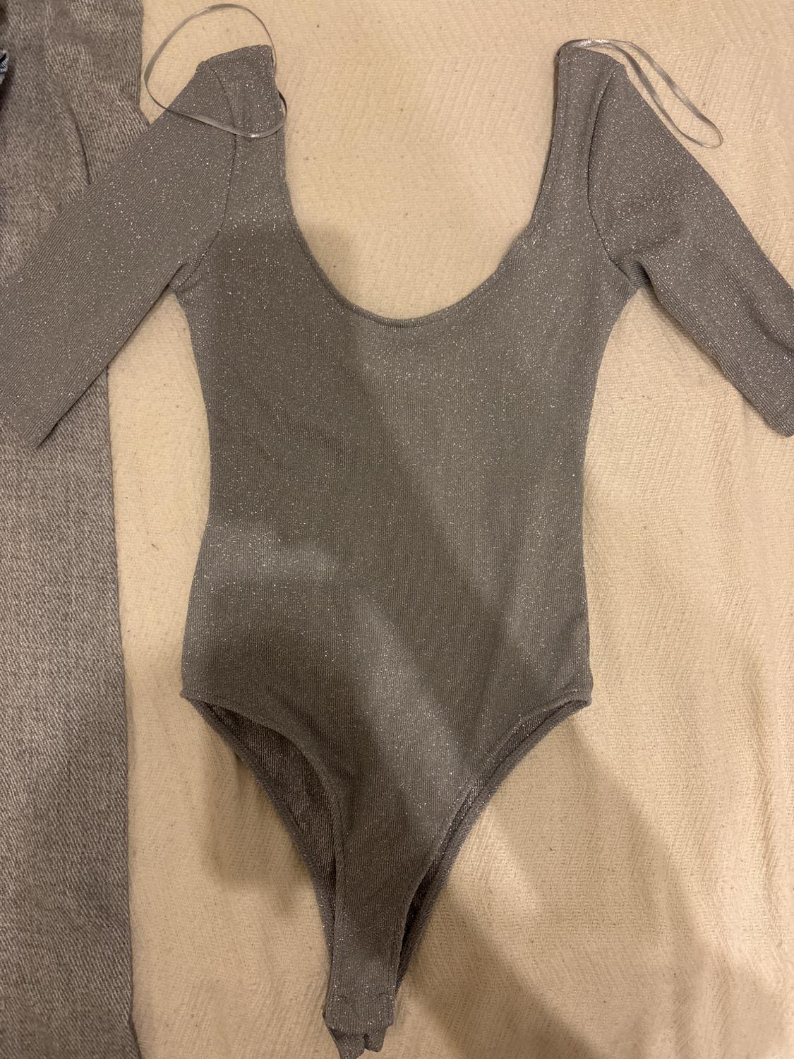 Shiny grey long-sleeved bodysuit on a beige surface, with thin straps visible on the shoulders.