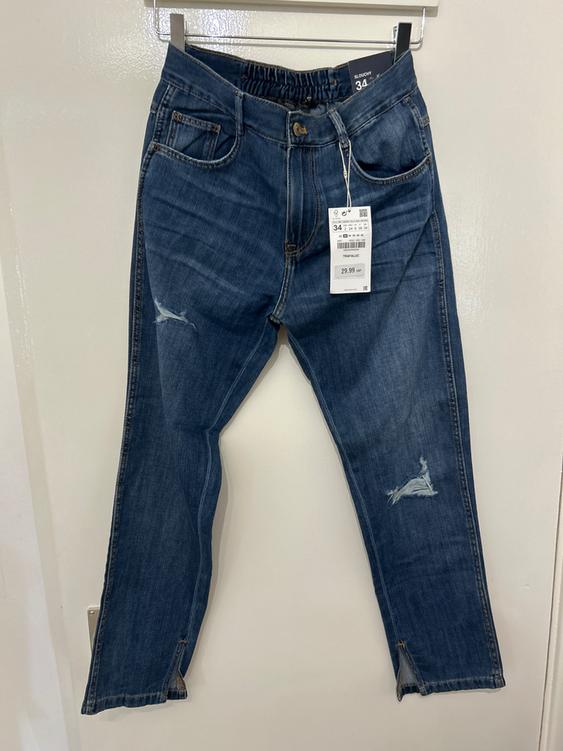Worn blue jeans hanging on a white hanger. Visible tag with price of 29.99 and size 34. Neutral setting.