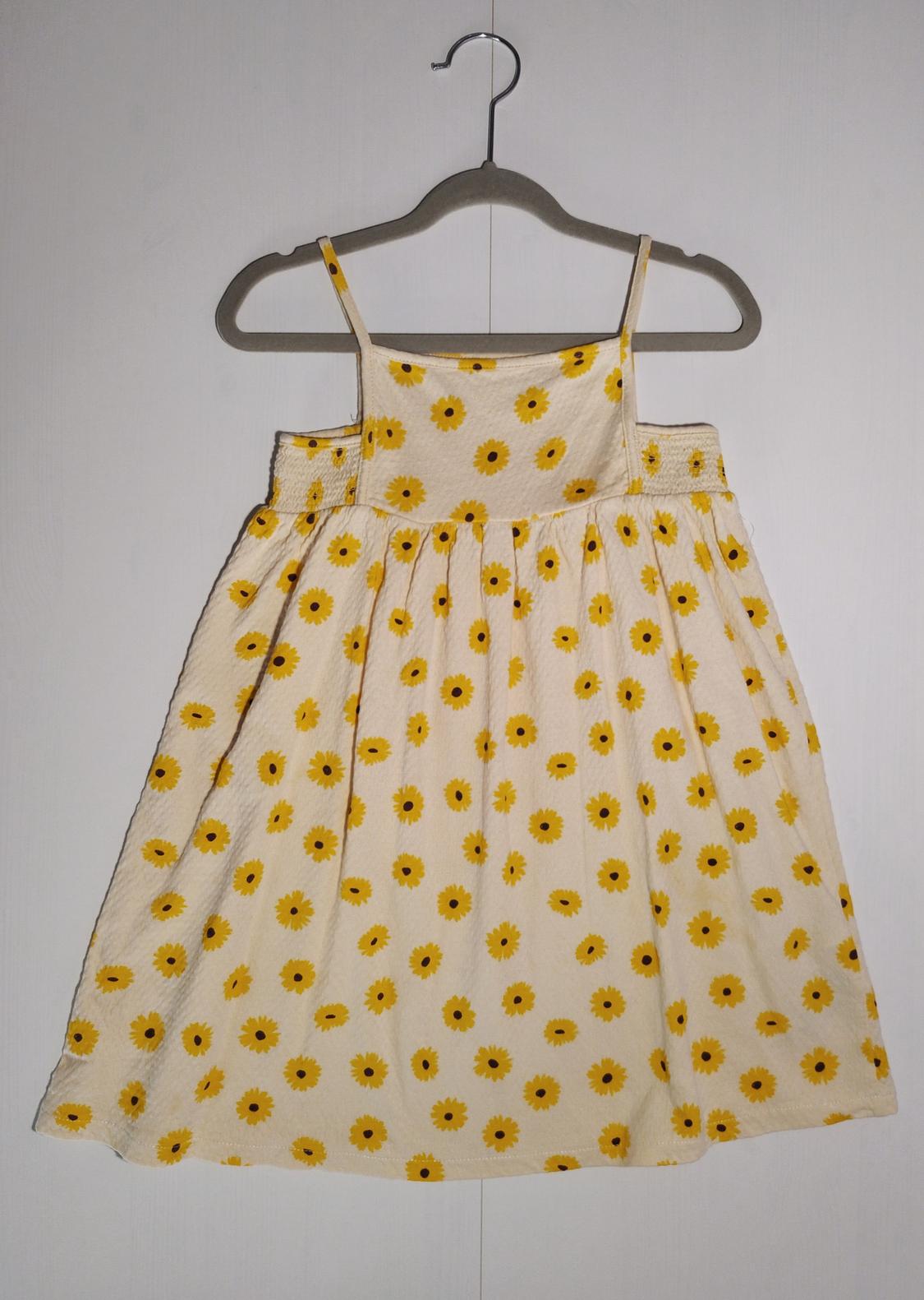 Child's sundress with yellow sunflower print on a white background, hanging on a grey hanger.