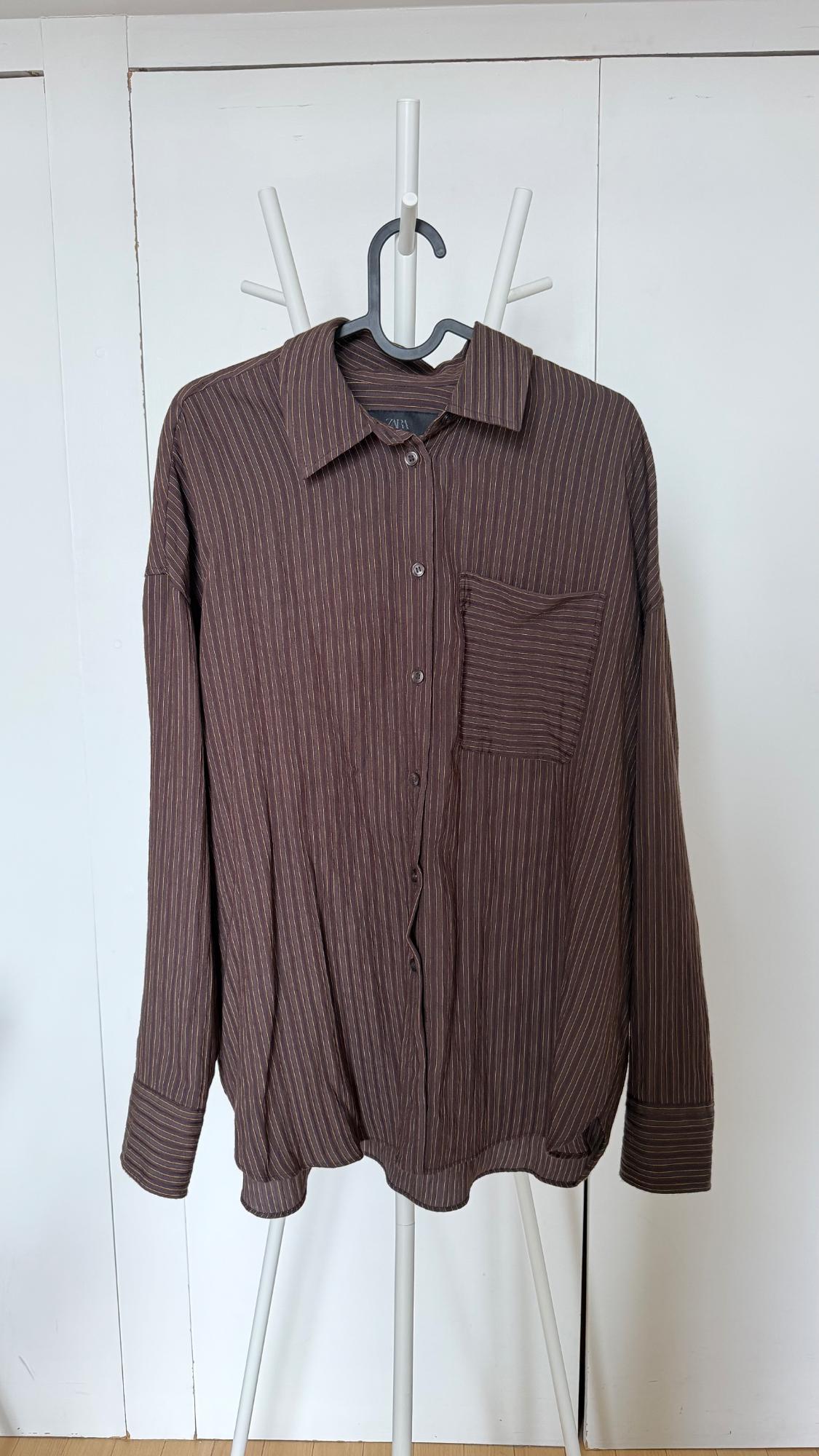 Brown long-sleeved shirt with vertical stripes and a chest pocket, hanging on a white clothes rack. Label with the text Zara.