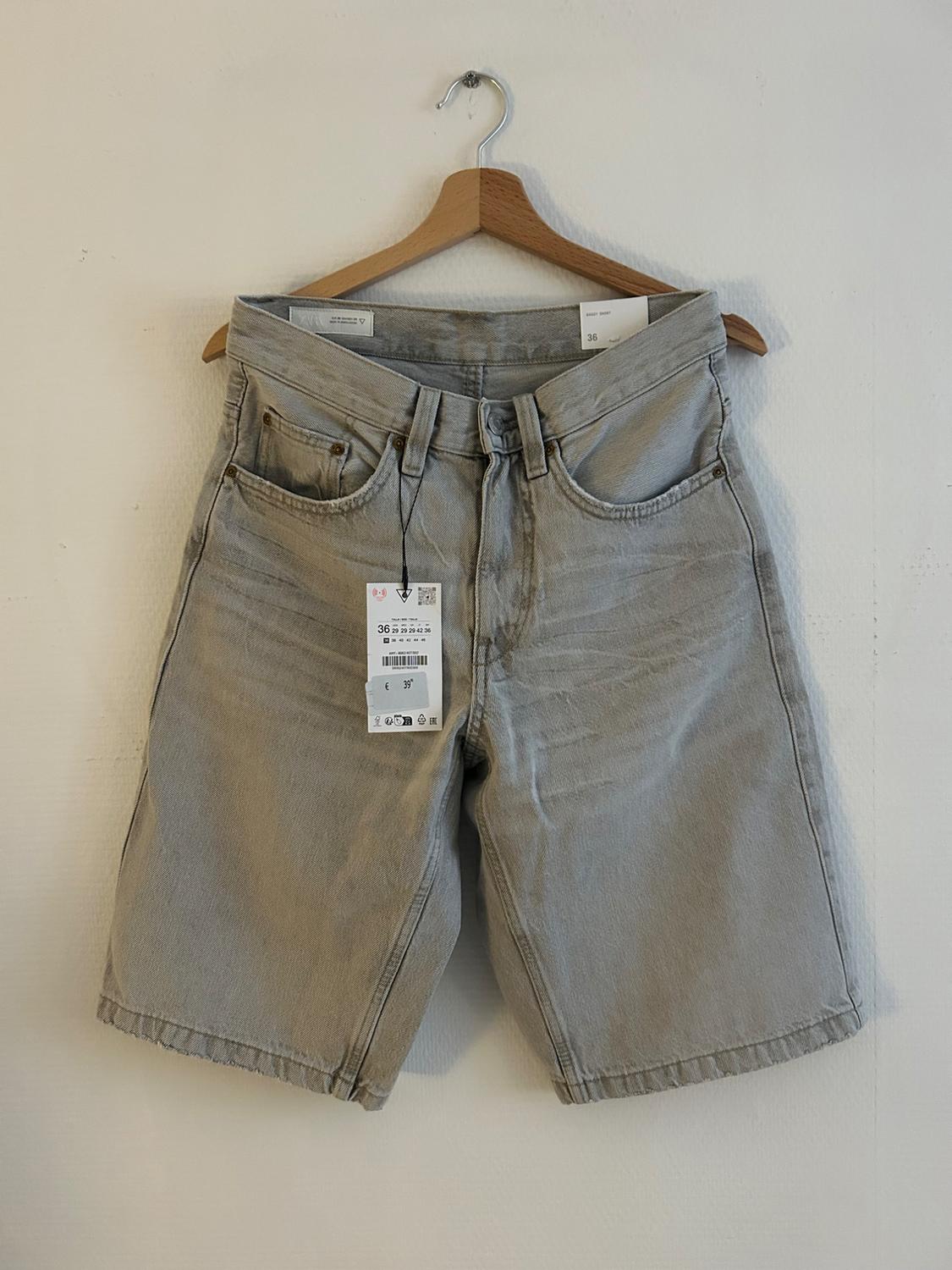 Light grey denim shorts hanging on a wooden hanger, with size 36 label visible on the front.