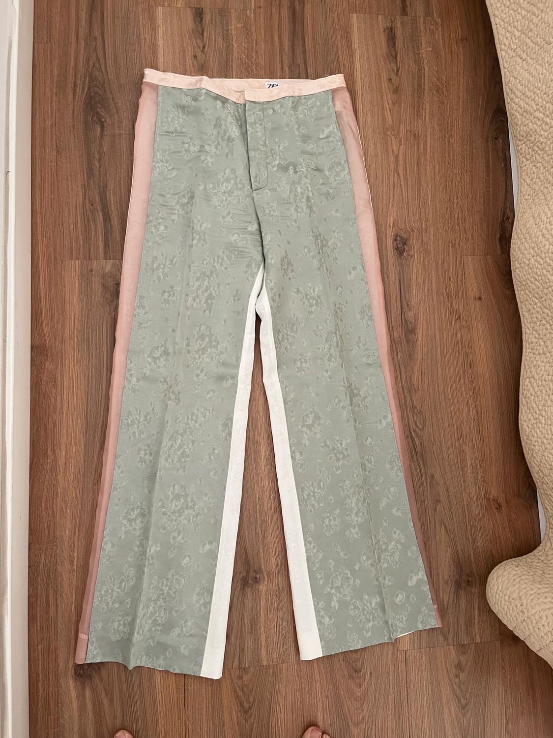 Patterned fabric trousers in shades of green, pink, and white, placed on a light wooden floor.