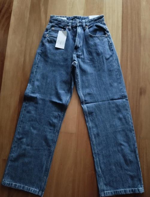 Blue wide-leg jeans with a white hang tag, laid on a wooden floor.
