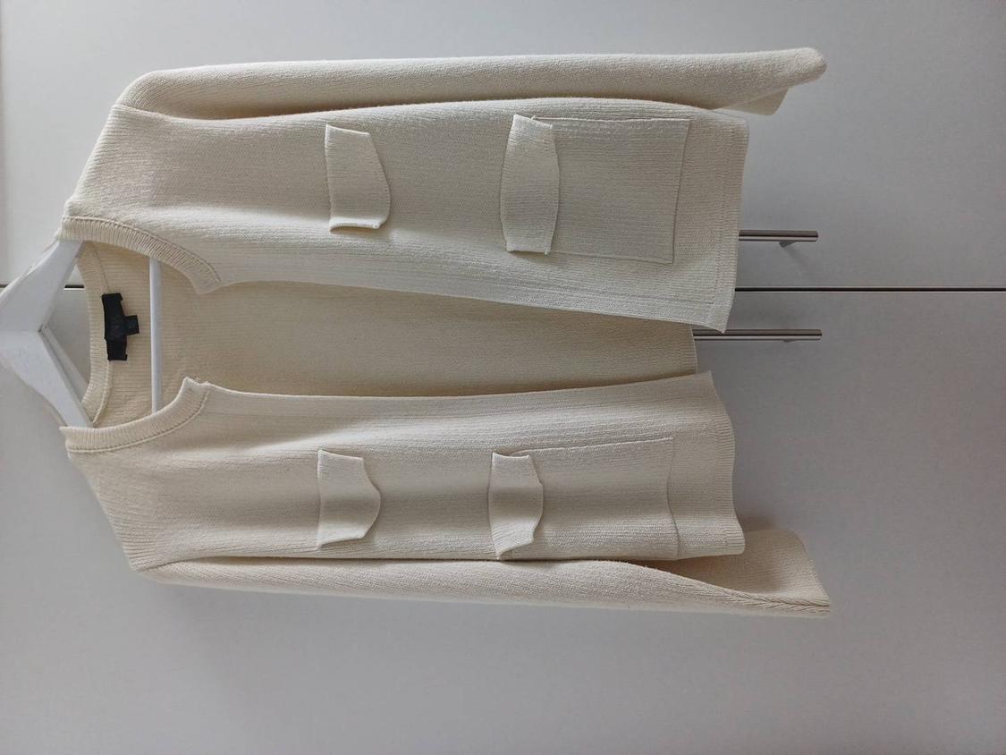 Beige textured fabric jacket hanging on a white hanger, with large front pockets and a white background.