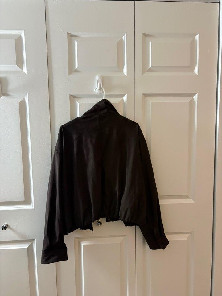 Dark jacket with an elasticated hem hanging on a hook on a white panelled door. Simple composition with a relaxed atmosphere.
