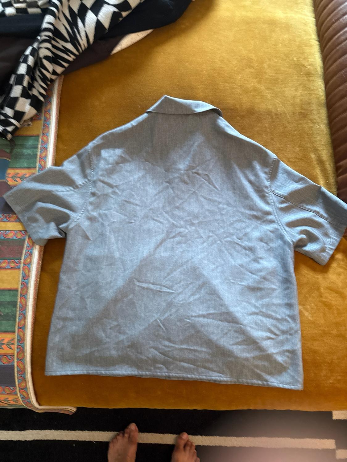 Back of a short-sleeved blue shirt on a mustard sofa. Relaxed atmosphere with patterned fabrics and bare feet.