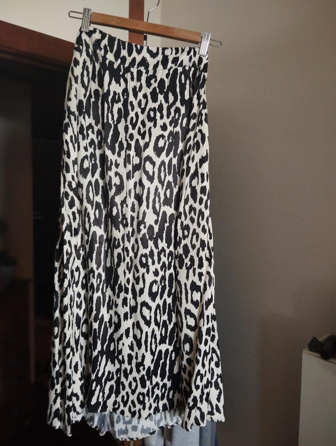 Μακριά φούστα με ασπρόμαυρο animal print κρεμασμένη σε ξύλινη κρεμάστρα με μανταλάκια σε έναν εσωτερικό χώρο με χαλαρή ατμόσφαιρα.