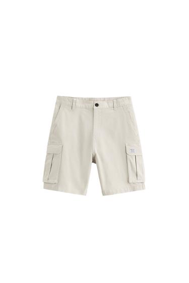 Elastic waistband shorts. Front pockets and back flap pockets. Flap patch pockets at legs. Front zip and button closure.