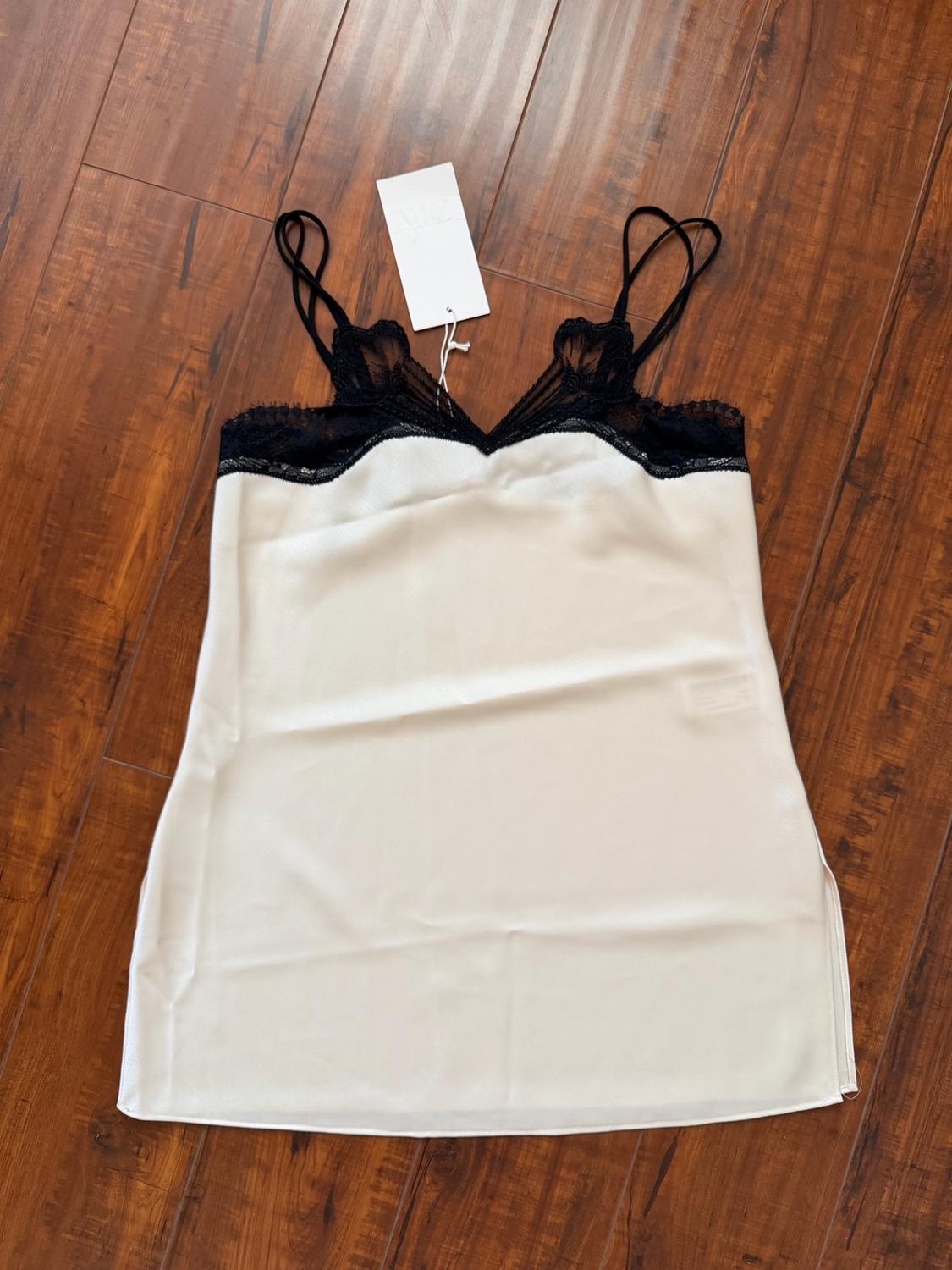 White slip dress with double straps and black lace on the neckline, photographed on a wooden floor.