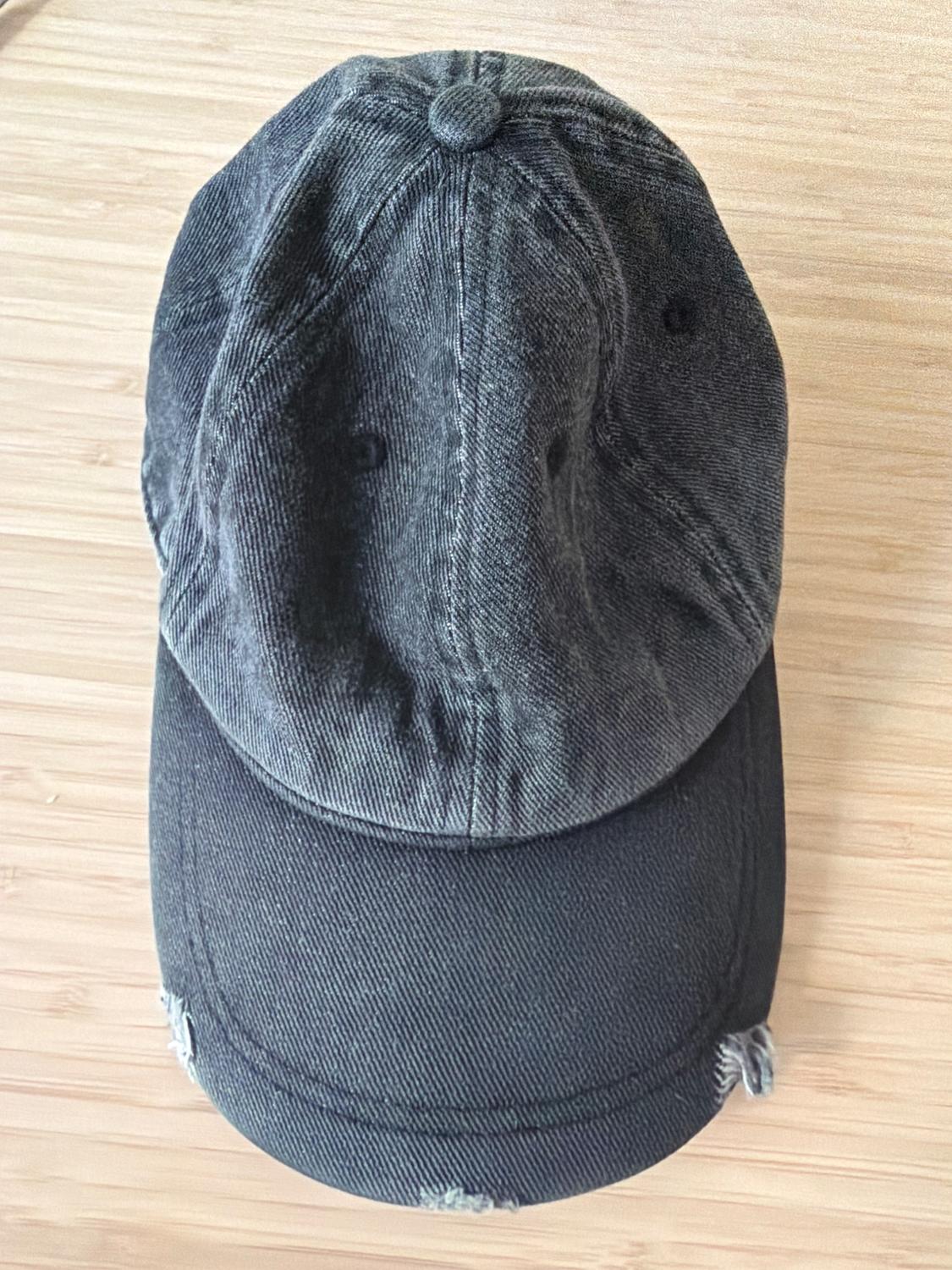 Worn black denim cap on a light wooden background, top view.
