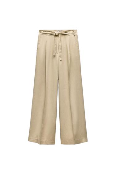 Front view of beige trousers with belt and side pockets.