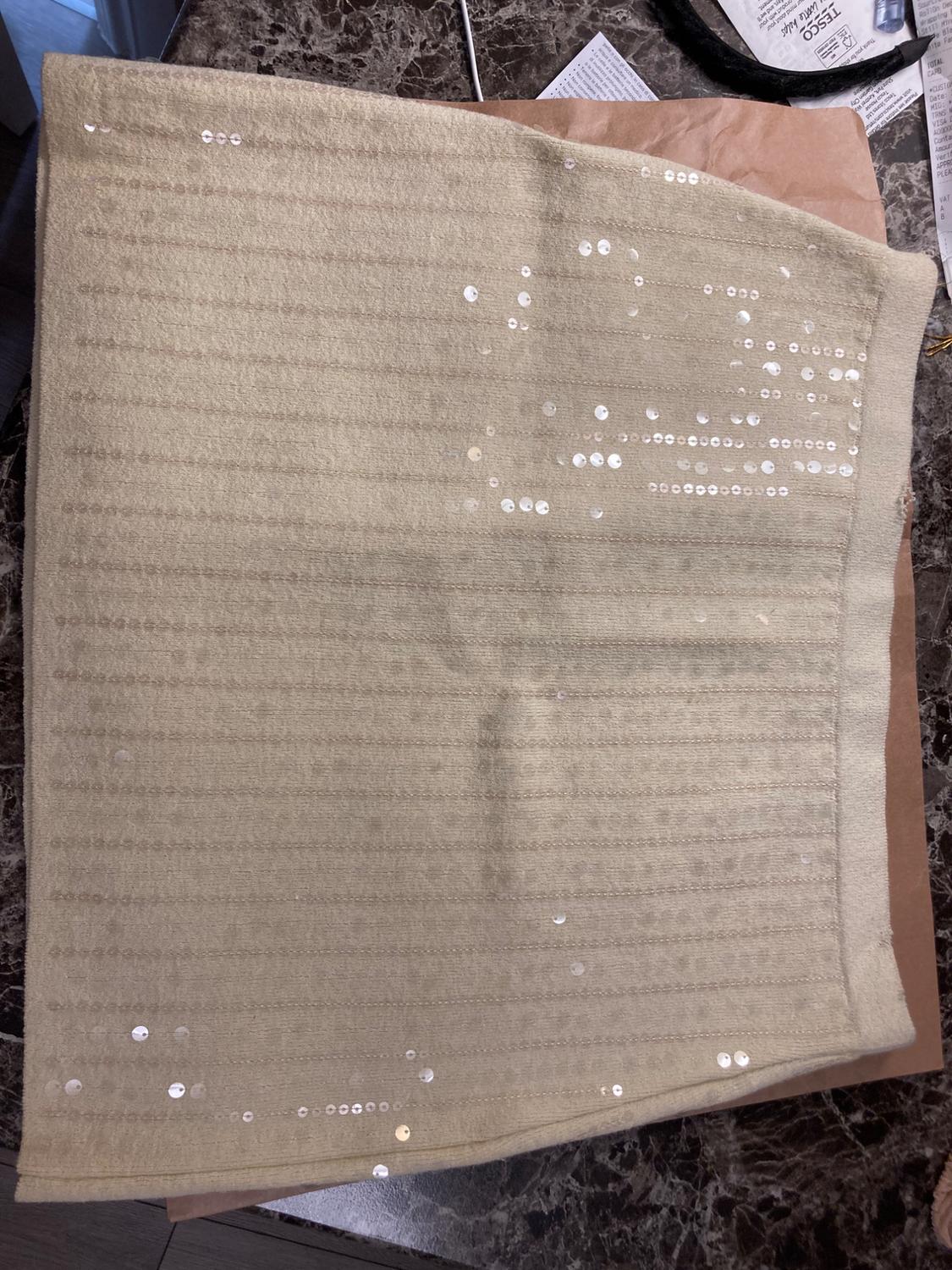 Beige skirt with sparkly sequins on a dark marble surface. Background with indistinct papers and objects.