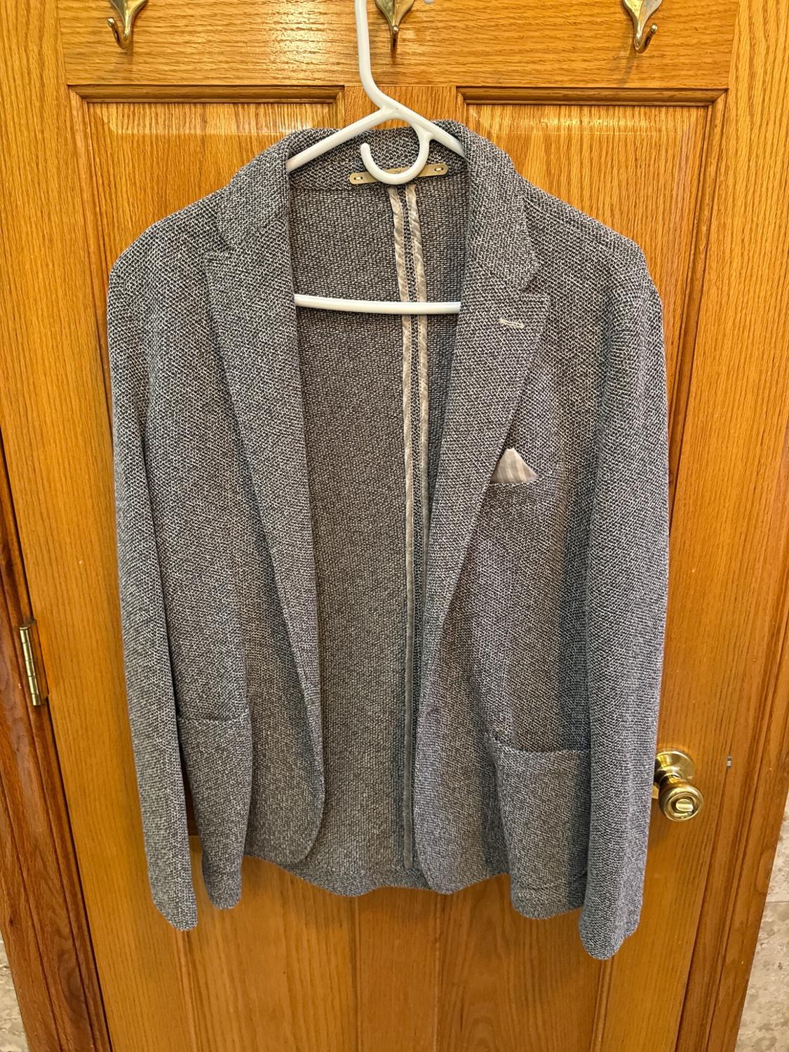 Textured grey blazer with a pocket square, hanging on a white hanger over a wooden door in an everyday setting.