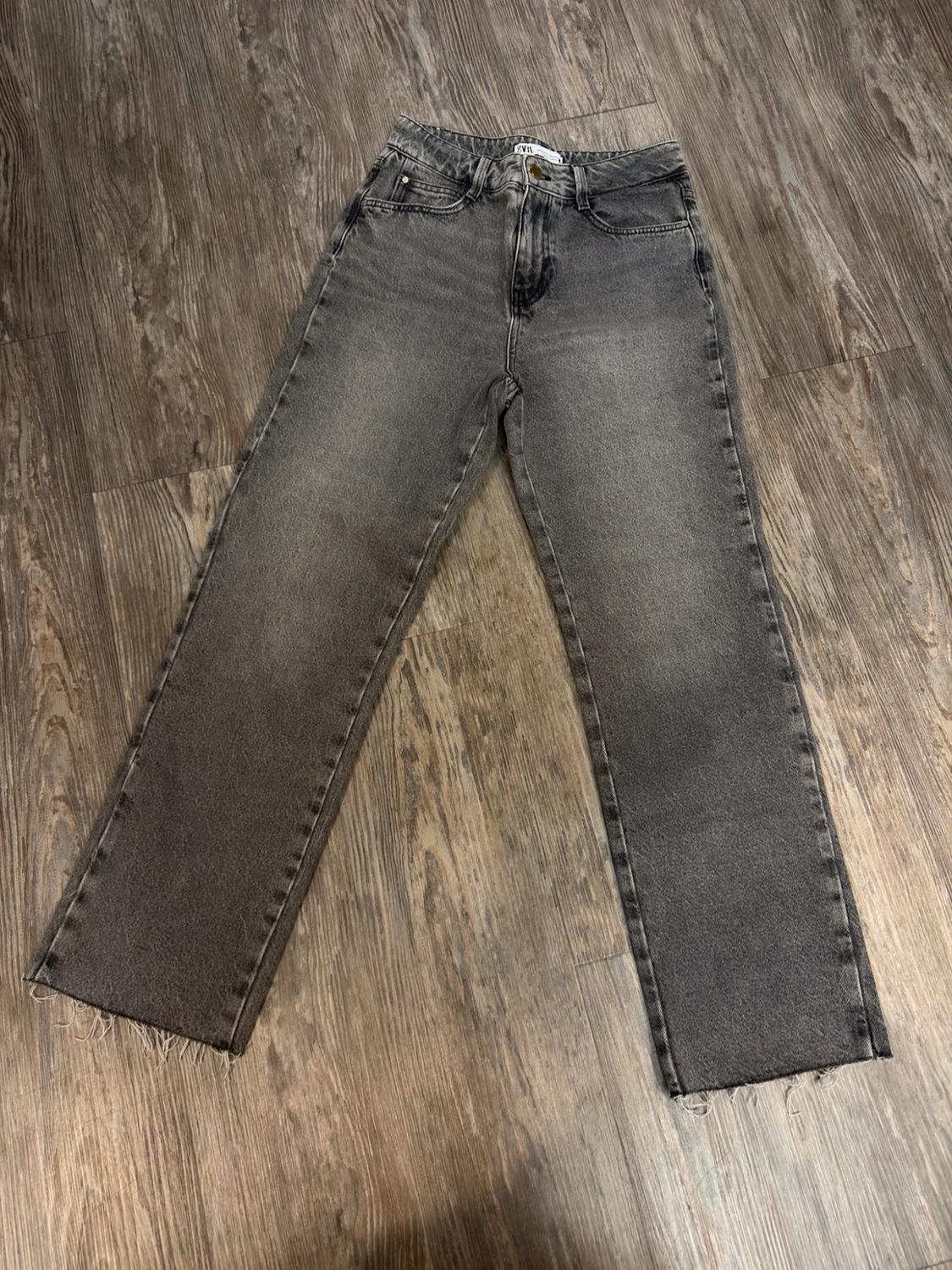 Dark gray straight-leg jeans with a frayed hem, photographed flat on a wooden floor.