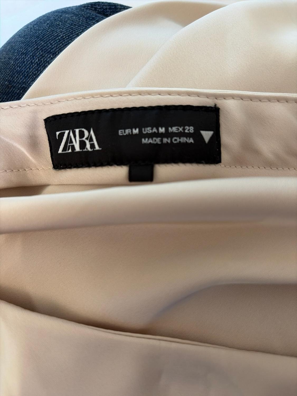 Black label on beige fabric. Text: ZARA EUR M USA M MEX 28 MADE IN CHINA. Blue denim fabric detail.