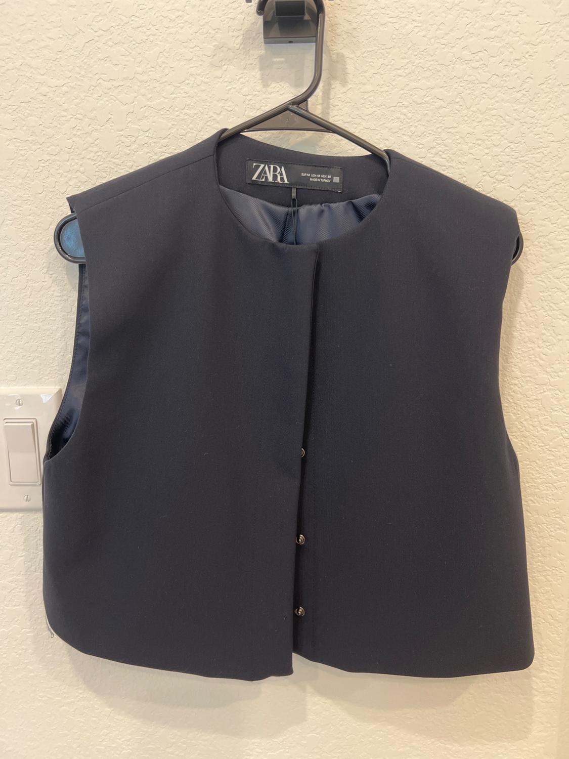 Zara black sleeveless vest hanging on a black hanger against a light-colored wall. Label visible on the inside of the collar.