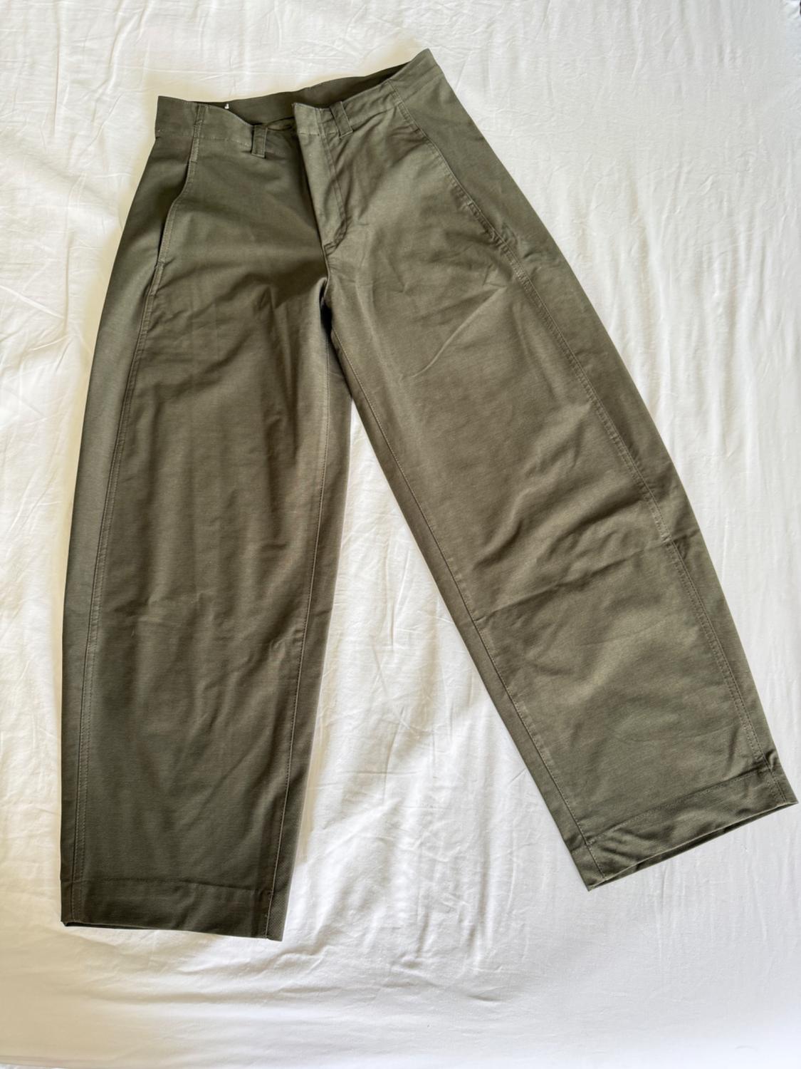 Olive green wide-leg casual trousers, laid out on a wrinkled white fabric background. The seams on the legs stand out.