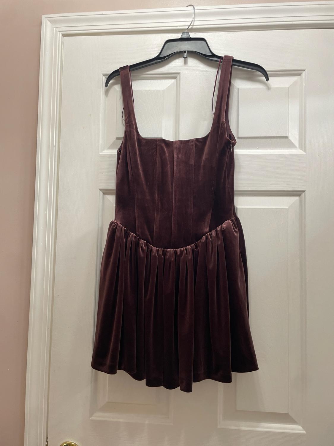 Short dark brown velvet dress with a square neckline, fitted bodice, and gathered skirt, hanging on a white door.