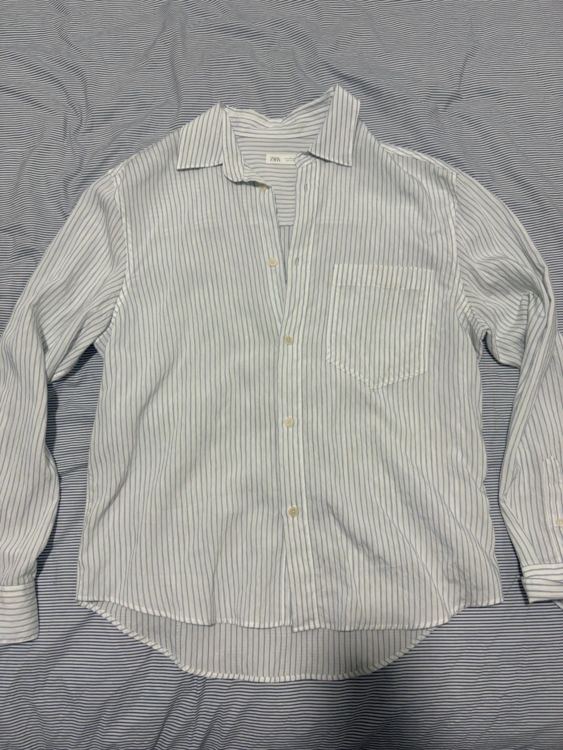 White and blue striped shirt with a chest pocket, on a matching fabric surface with the same striped pattern.