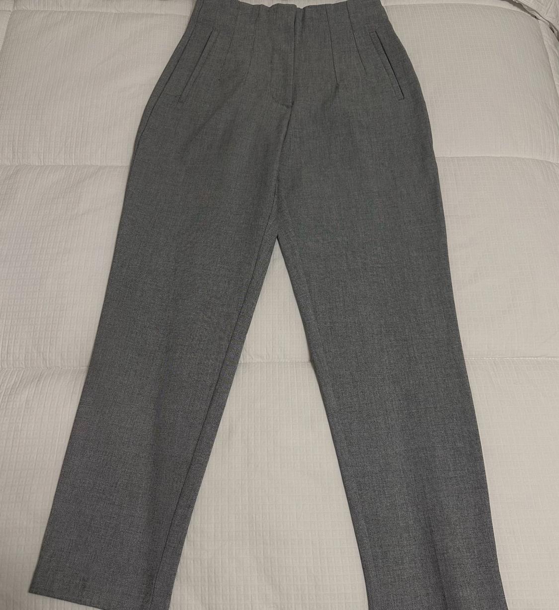 Gray dress pants with pleats and side pockets, laid out on a padded white surface.