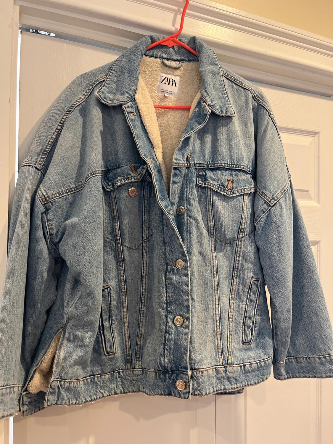 A light blue denim jacket with a wool interior, hanging on a red hanger. The visible label shows the ZARA brand.