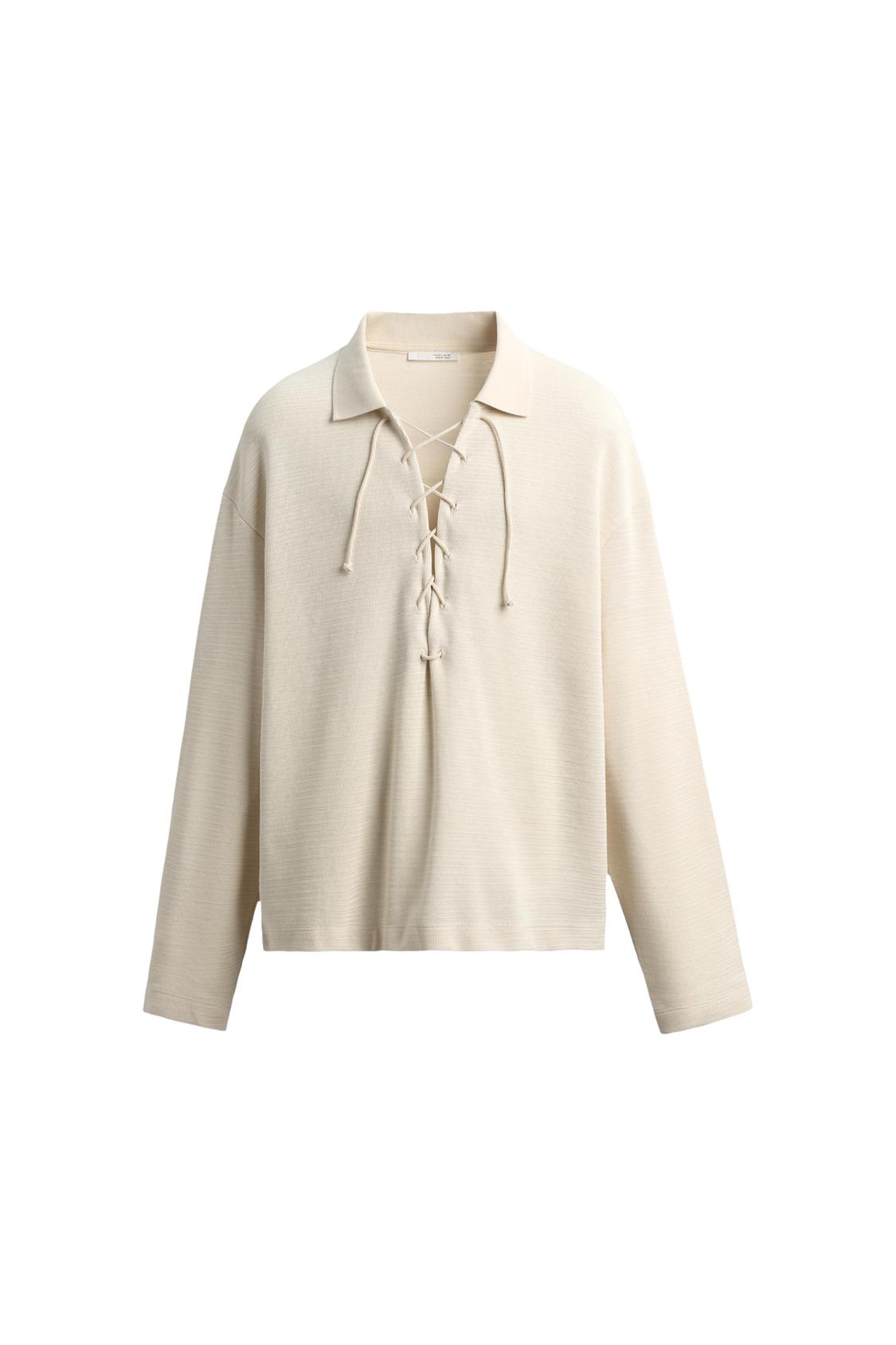 Beige long-sleeved shirt with a collar and lace-up closure on the chest,
against a white background.