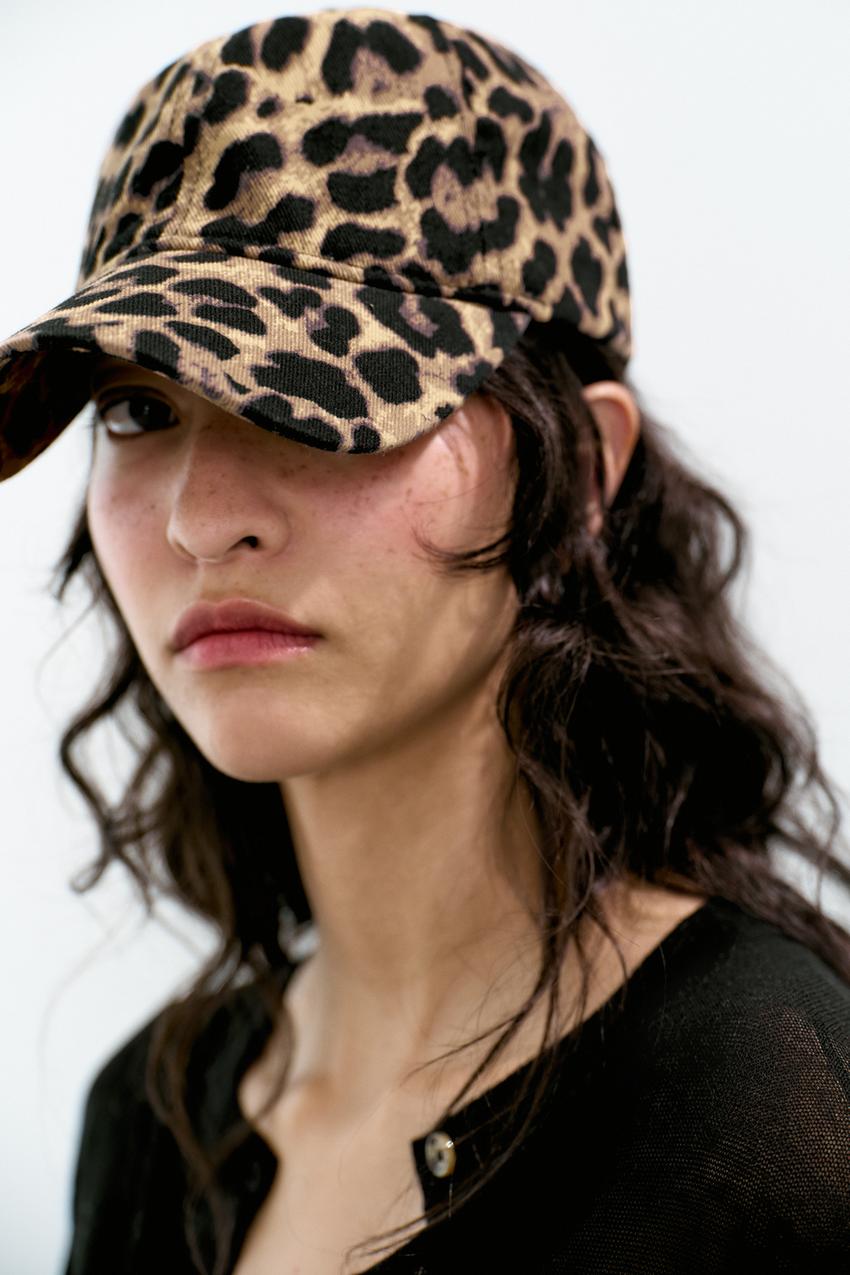Close-up of a leopard print cap with a curved brim, paired with a black button-front top.