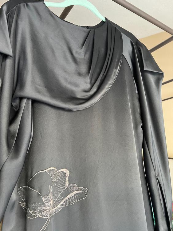 Black satin dress hanging on a green hanger, with an embroidered flower design on the bottom.
