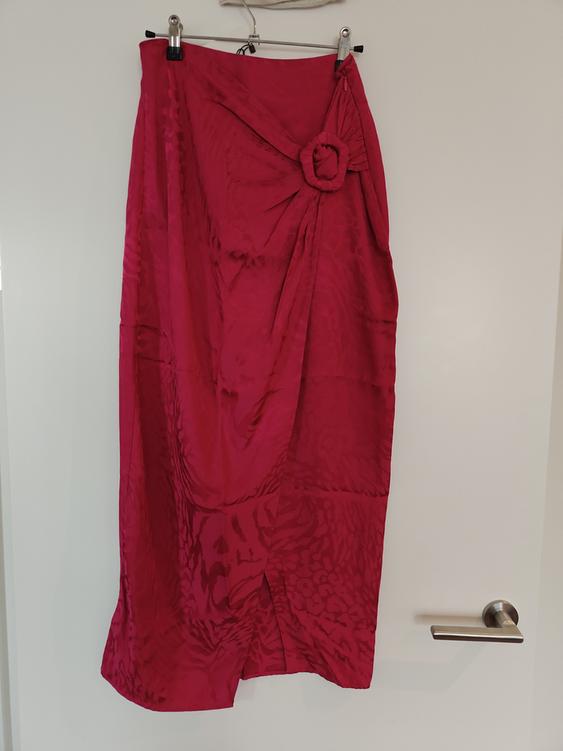 Red textured long skirt with a knot detail at the waist, hanging on a hanger over a white door.
