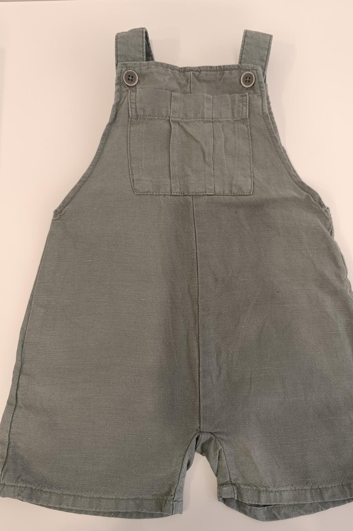 Front view of a pair of short grey dungarees with straps and buttons on the upper front.
