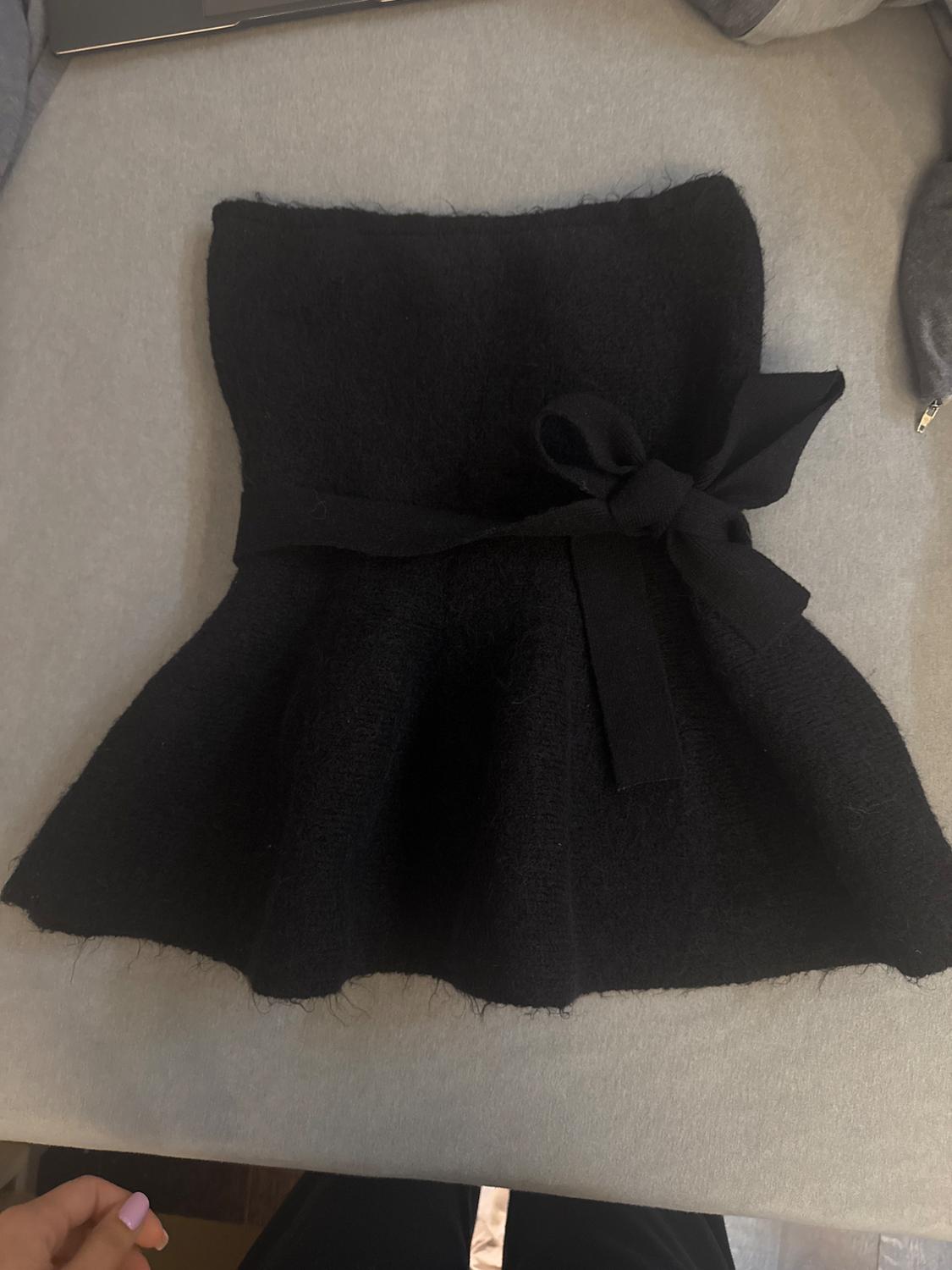 Black wool skirt with tie belt on a grey surface. Flared hem and soft texture.