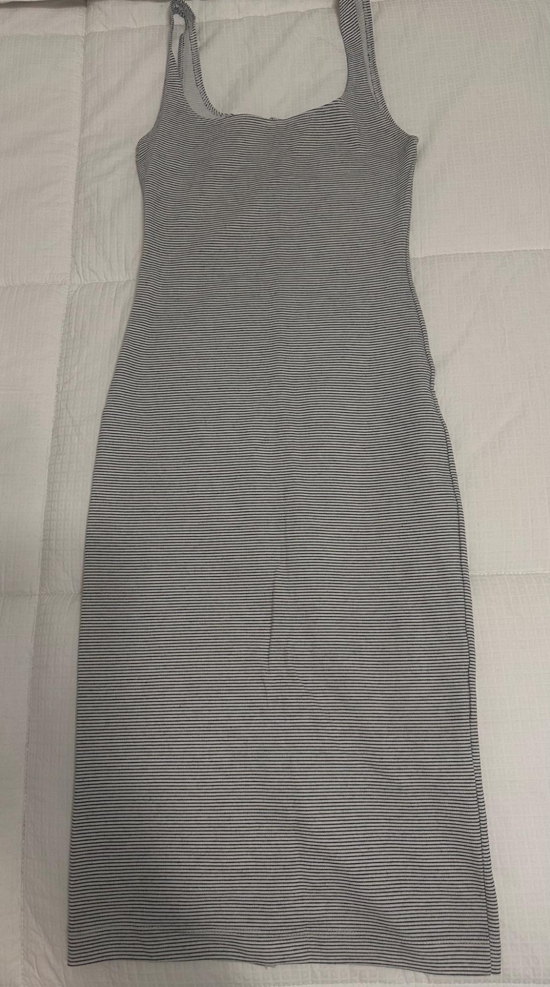 Sleeveless bodycon dress with thin horizontal stripes, laid out on a white quilted bedspread. Casual and relaxed style.
