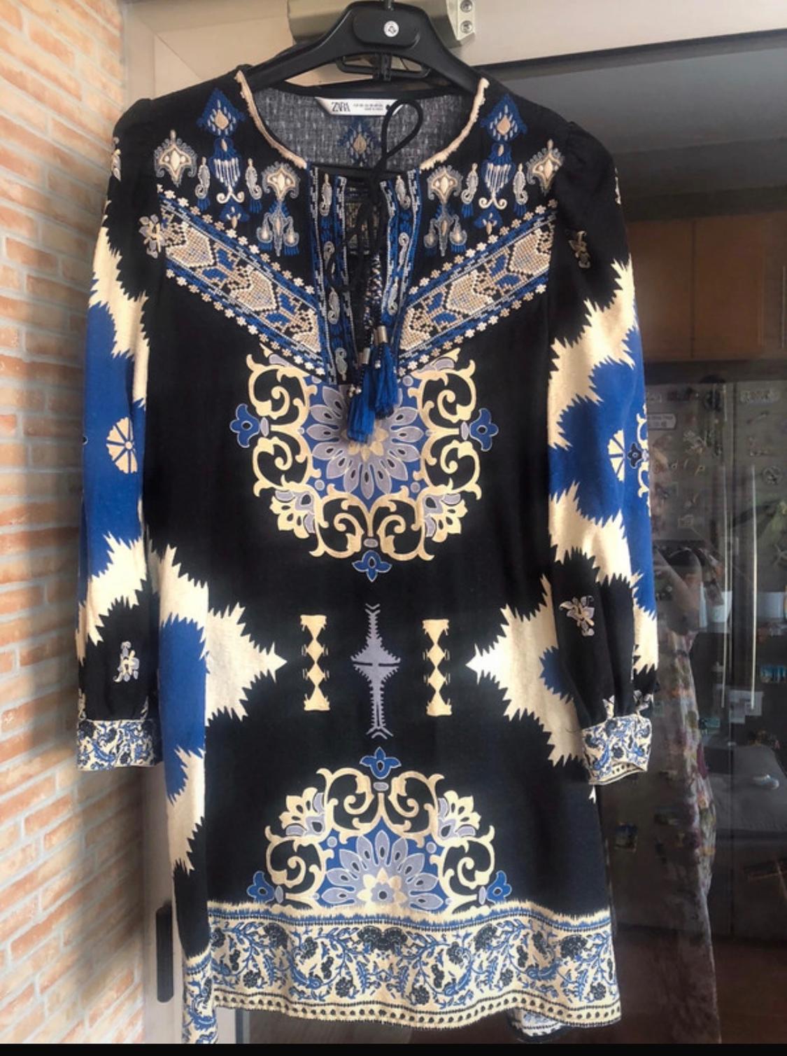 Halter-neck dress with geometric print in blue, black, and beige. Floral and embroidered details on the collar and sleeves.