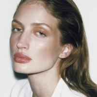 Image 29: Close-up of a model with loose hair and natural makeup, wearing a white blouse, on a white background.