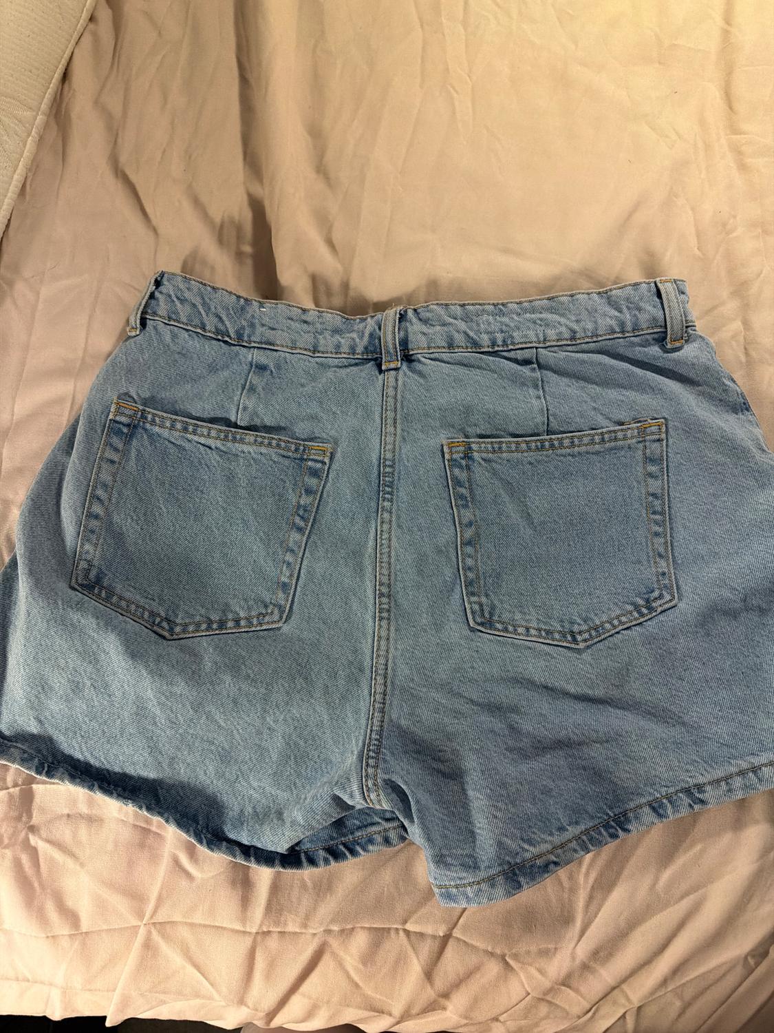 Light blue denim shorts with back pockets, placed on a crumpled beige quilt.